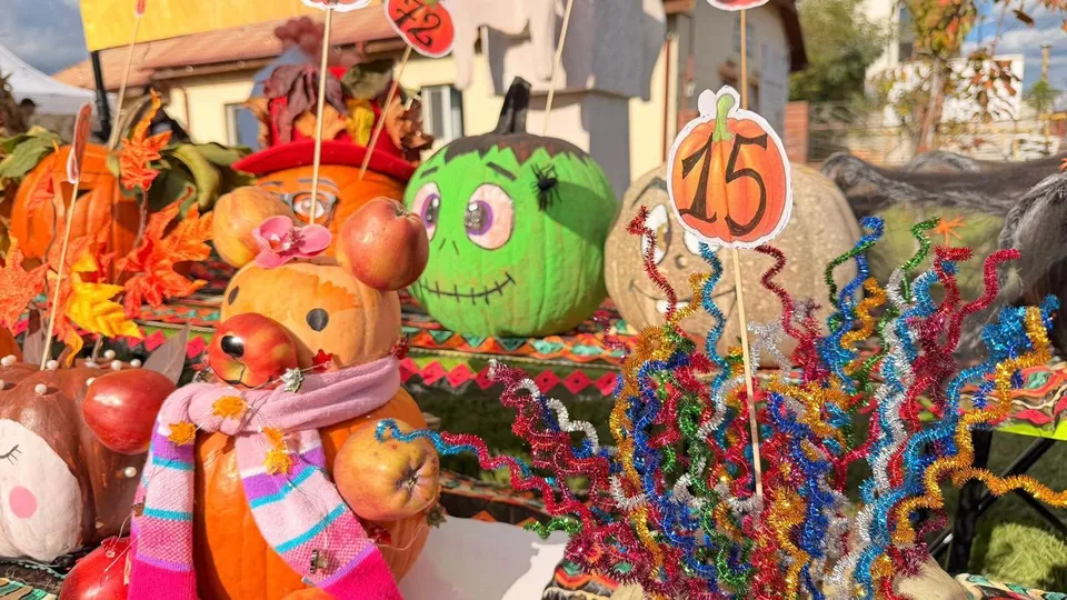 Diverse dovleci decorați cu fețe desenate și accesorii colorate sunt așezați pe o masă lângă decorațiuni festive din sârmă colorată.