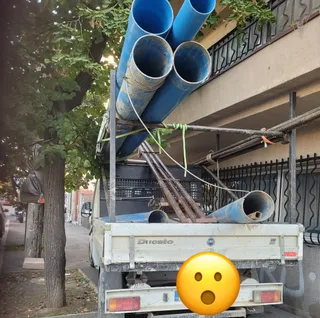 O autoutilitară albă transportă mai multe țevi și tuburi de culoare albastră în partea din spate.
