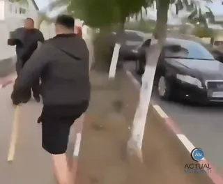Un bărbat cu hanorac negru și pantaloni scurți este surprins în mișcare pe un trotuar lângă mașini parcate.