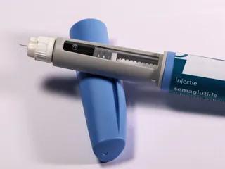 Un dispozitiv de injecție cu semaglutidă este așezat pe un obiect cilindric albastru pe un fundal alb.