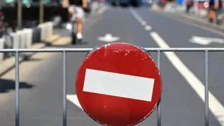 Un semn de circulație circular, roșu cu o bară alb horizontală, este montat pe un gard metalic în fața unei străzi asfaltate.