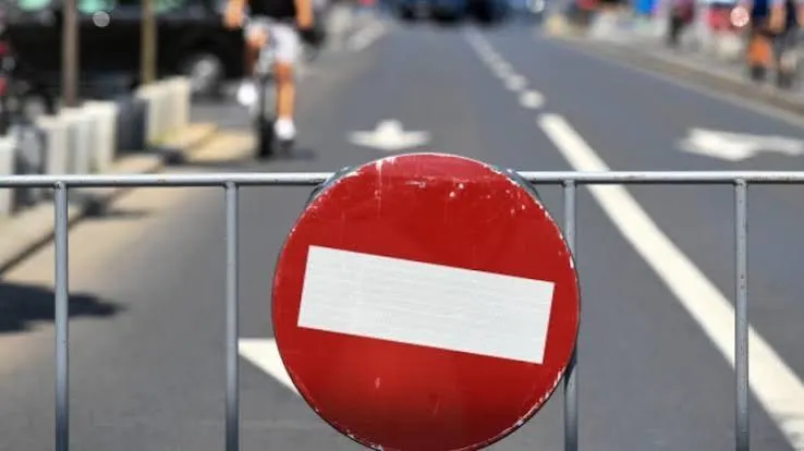 Un semn de circulație circular, roșu cu o bară alb horizontală, este montat pe un gard metalic în fața unei străzi asfaltate.