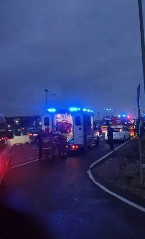 Vehicule de intervenție cu lumini albastre aprinse sunt oprite pe un drum asfaltat sub un cer închis.