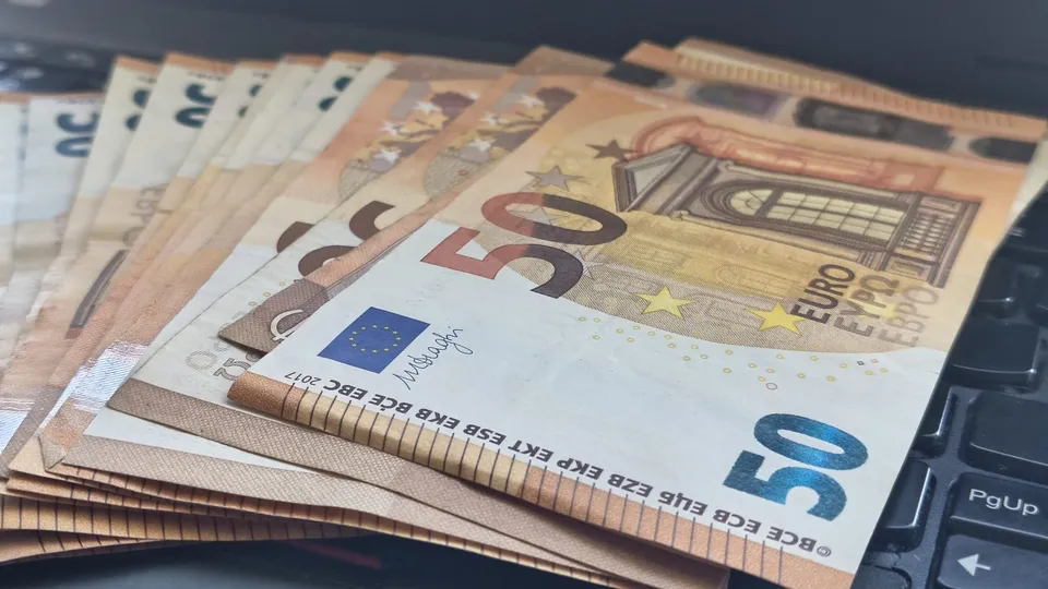 Mai multe bancnote de cincizeci de euro sunt întinse pe un tastatură de laptop întunecată.