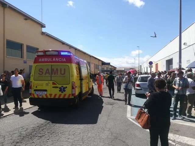 O ambulanță galbenă cu inscripția SAMU stă pe un drum asfaltat lângă un grup de oameni sub un cer senin.