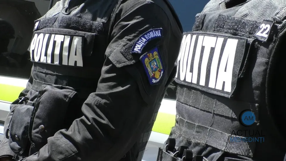 Doi polițiști români, îmbrăcați în uniforme negre cu veste tactice, sunt fotografiați de la brâu în sus, cu insigna "POLIȚIA ROMÂNĂ" vizibilă.