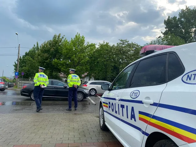 Doi polițiști în uniforme galben-verzui stau pe o stradă lângă un autoturism negru și o mașină de poliție albă.