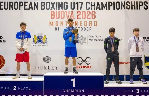 Patru tineri sportivi stau pe podiumul unui podium de premiere, cel din centru ținând un trofeu de culoare aurie.