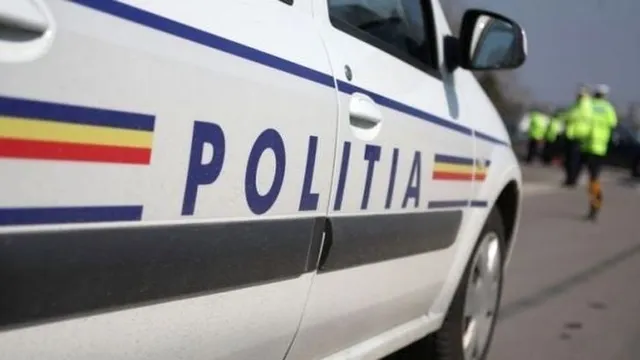 O mașină de poliție albă cu inscripția "POLIȚIA" și dungi tricolore pe lateral, cu un polițist în fundal.