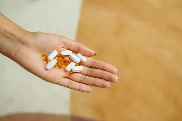 O mână deschisă ține câteva capsule albe și capsule mici, rotunde, de culoare galbenă.