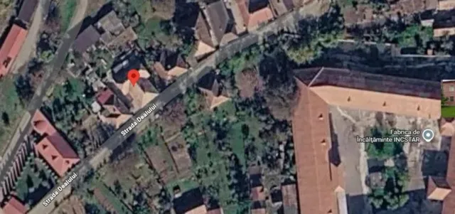 O vedere aeriană de sat arată o stradă cu case, curți verzi și un punct de marcaj roșu pe un acoperiș.