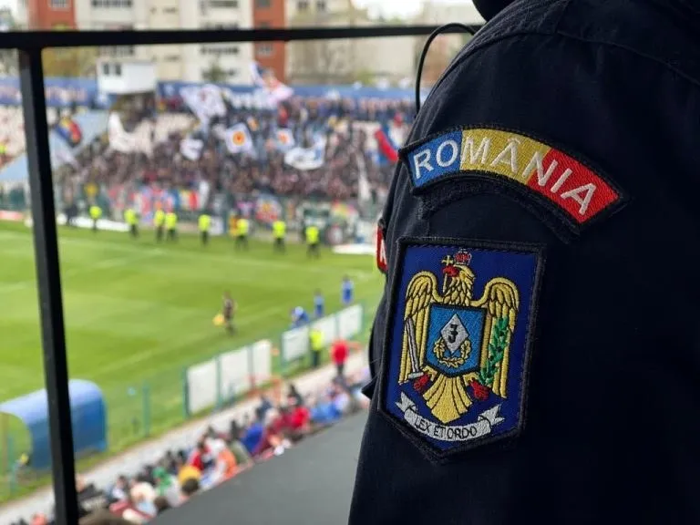 Un uniformat de spatele este prezentat cu un patch de România și un emblema pe umăr, în timp ce un stadion cu mulțime este în fundal.