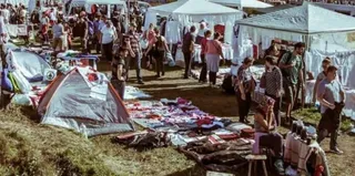 O mulțime de oameni se află într-un câmp deschis lângă corturi albe și obiecte întinse pe iarbă.