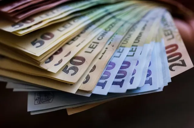 Un teanc de bancnote de diferite valori este întins pe o suprafață întunecată.