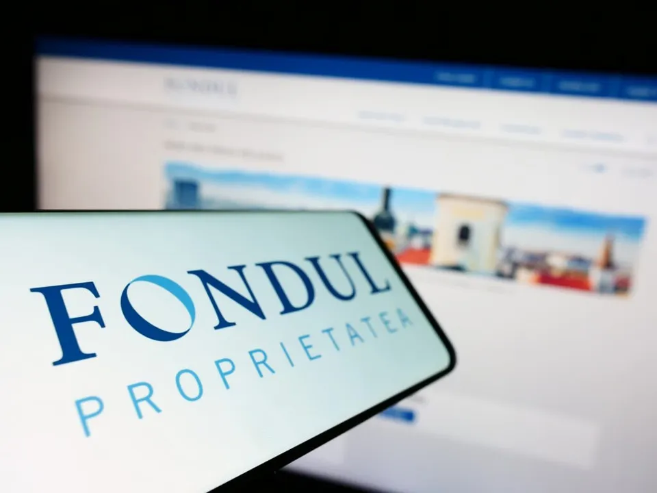Un ecran de smartphone afișează textul albastru pe fundal alb, în timp ce un monitor de calculator este vizibil în fundalul neclar.