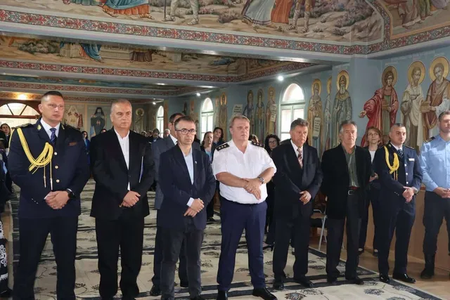 Un grup de bărbați stă în picioare în fața unui perete pictat cu figuri religioase într-o încăpere cu tavan înalt.