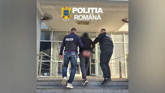 Trei polițiști în uniformă neagră cu inscripții albe transportă un bărbat care poartă pantaloni scurți și este văzut din spate în fața unei clădiri.