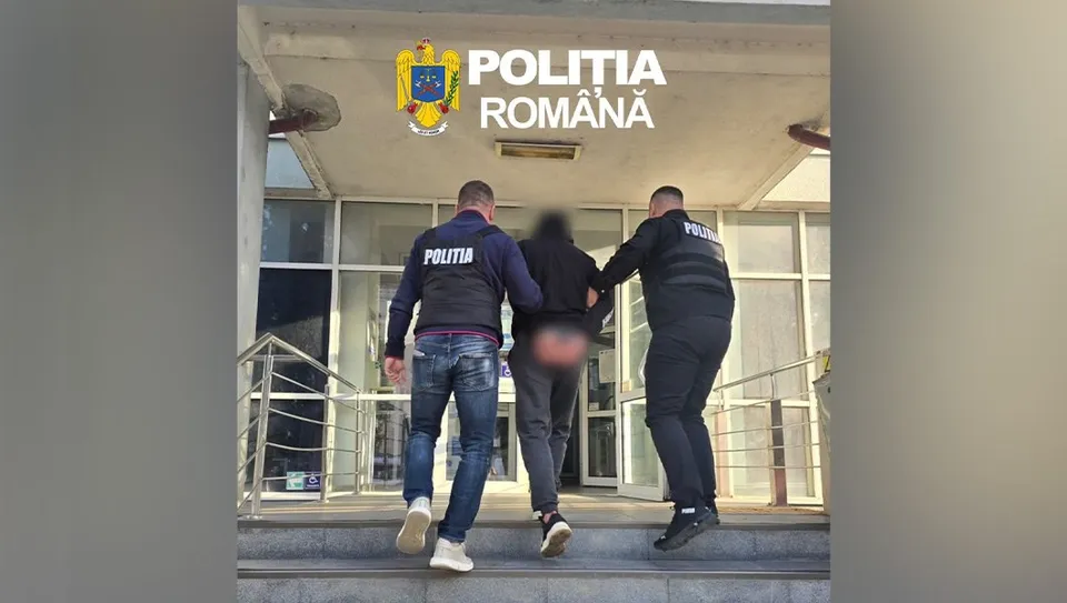 Trei polițiști în uniformă neagră cu inscripții albe transportă un bărbat care poartă pantaloni scurți și este văzut din spate în fața unei clădiri.