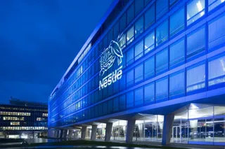 O clădire modernă cu fațadă de sticlă iluminată în albastru prezintă un logo Nestlé pe partea superioară.