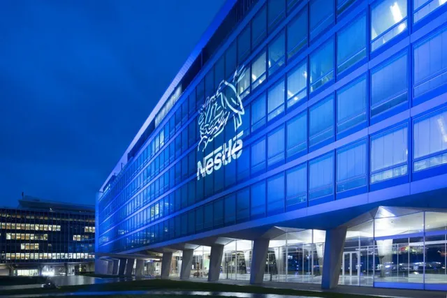 O clădire modernă cu fațadă de sticlă iluminată în albastru prezintă un logo Nestlé pe partea superioară.