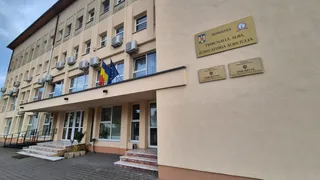 O clădire cu ferestre și plăcuțe informative pe perete, având un pridvor cu scări și steaguri afișate pe fațadă.
