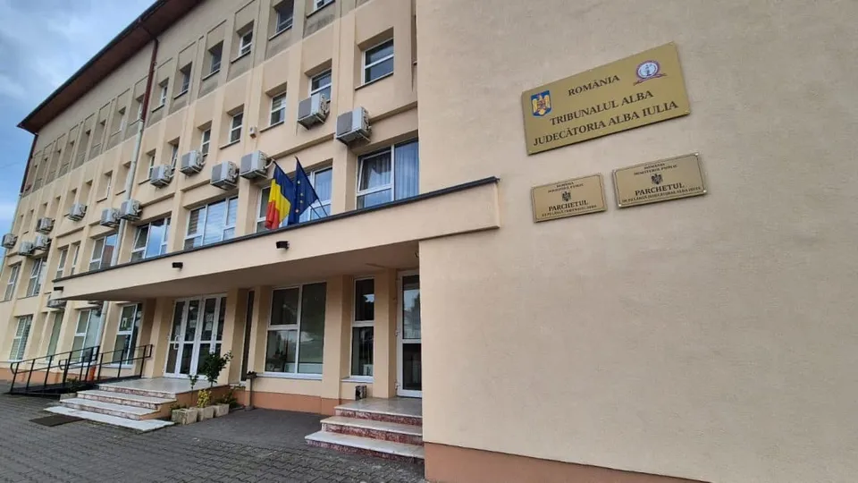 O clădire cu ferestre și plăcuțe informative pe perete, având un pridvor cu scări și steaguri afișate pe fațadă.
