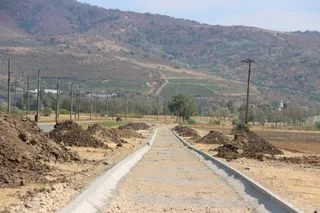 O cale pietruită cu borduri de beton se întinde spre un deal împădurit sub un cer senin.