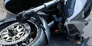 O motocicletă de culoare albă este întinsă pe asfalt, evidențiind roata din față, discul de frână și partea frontală a carcasei.