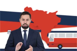 Un bărbat cu barbă, purtând costum închis la culoare și cravată, stă în fața unui fundal cu o siluetă roșie și un autocar stilizat.