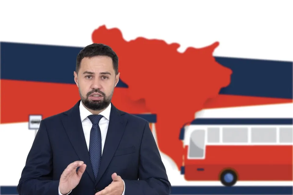Un bărbat cu barbă, purtând costum închis la culoare și cravată, stă în fața unui fundal cu o siluetă roșie și un autocar stilizat.