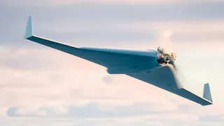 Un avion fără echipaj uman de culoare albă zboară pe un cer cu nori difuși sub lumina serii.