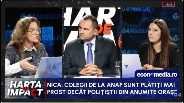Trei persoane stau la o masă într-un studio de televiziune, având în față laptopuri și un pahar cu apă.