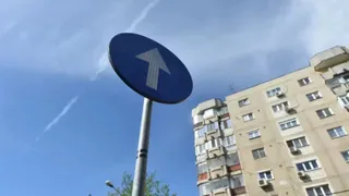Un semn circular albastru cu o săgeată albă orientată în sus este montat pe un stâlp metalic sub un cer înzăpezit.