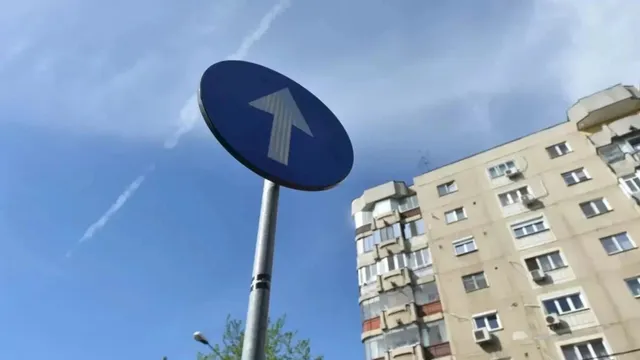 Un semn circular albastru cu o săgeată albă orientată în sus este montat pe un stâlp metalic sub un cer înzăpezit.