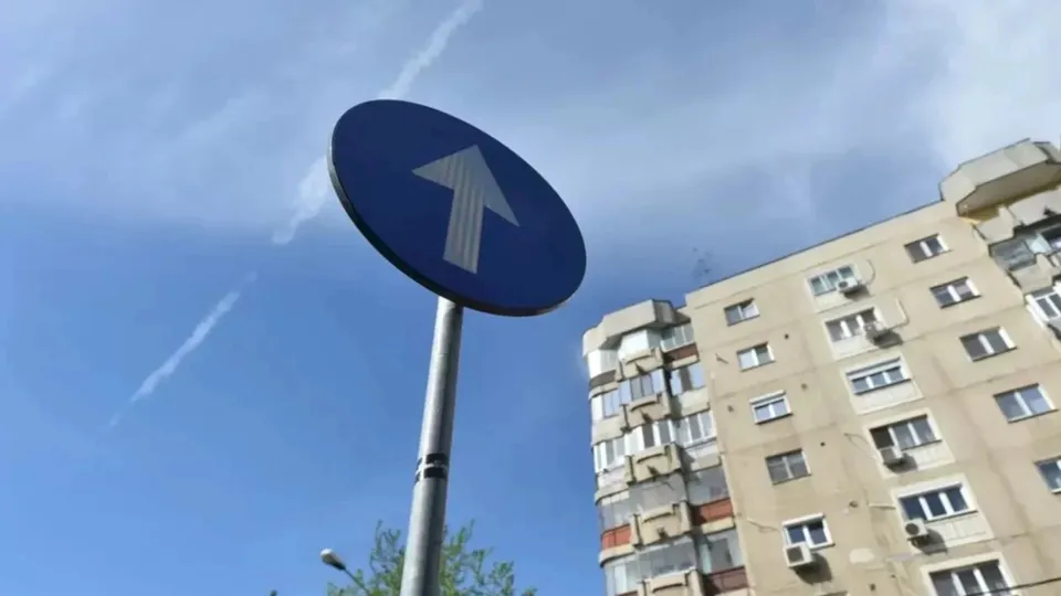 Un semn circular albastru cu o săgeată albă orientată în sus este montat pe un stâlp metalic sub un cer înzăpezit.