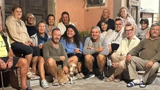 Un grup de persoane zâmbitoare stă împreună în fața unei clădiri, unele fiind așezate pe scaune, altele pe trepte.