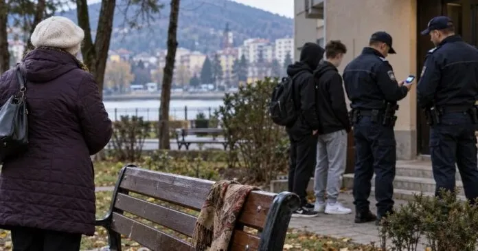 Trei bărbați în uniformă de polițist stau lângă doi tineri într-un parc, lângă un banc de lemn.