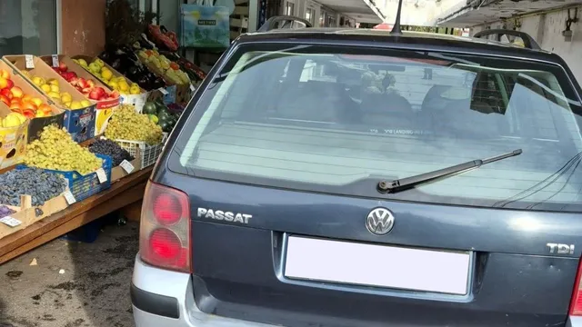 Spatele unui autoturism gri marca Volkswagen este parcat în fața unui stand cu fructe și legume colorate.