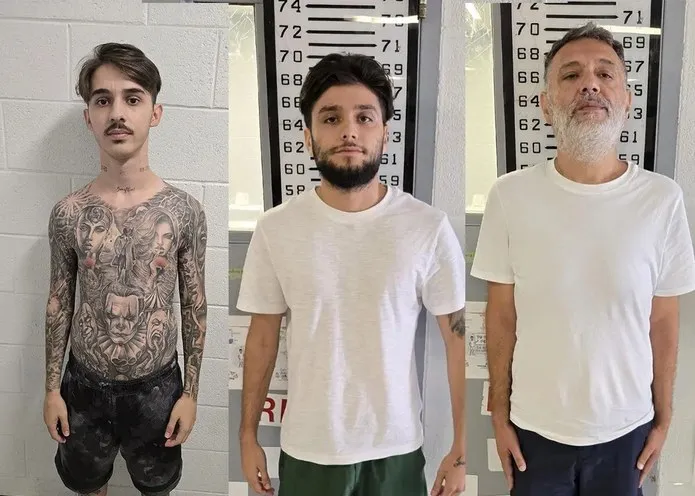 Trei bărbați stau în picioare în fața unor bare de măsurare, purtând tricouri albe și pantaloni scurți.