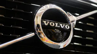 Un emblema circulară metalică cu textul VOLVO este montată pe o grilă de culoare neagră.