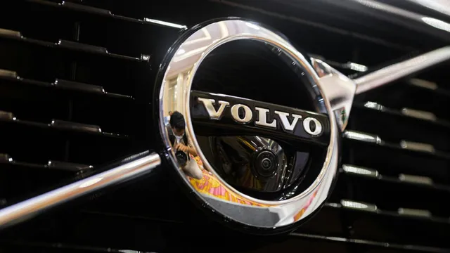 Un emblema circulară metalică cu textul VOLVO este montată pe o grilă de culoare neagră.