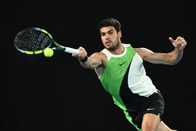 Un bărbat cu tricou alb și verde lovește o minge de tenis cu o racletă într-o poziție de mișcare pe un fundal negru.