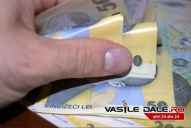 O mână ține și răsucește câteva bancnote de cincizeci de lei deasupra unei suprafețe pline cu bani.