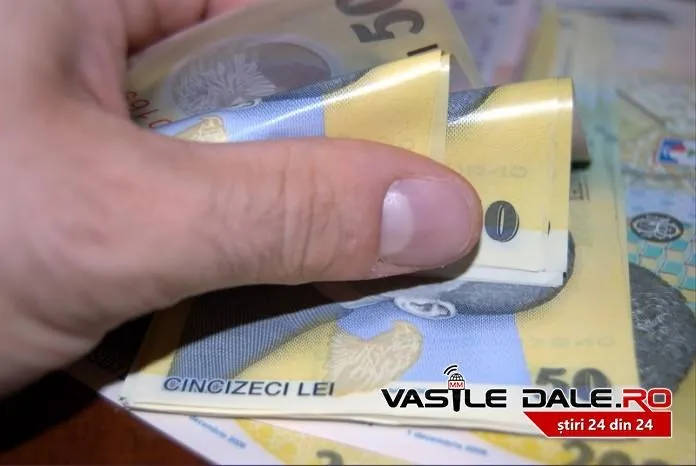 O mână ține și răsucește câteva bancnote de cincizeci de lei deasupra unei suprafețe pline cu bani.