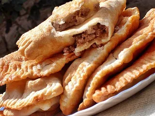 Mai multe produse de patiserie prăjite, cu margini zimțate și umplutură de carne, sunt așezate pe o farfurie albă.