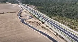 O vedere aeriană prezintă o autostradă cu mai multe benzi și o drum de bağlantă cu un sens giratoriu situat lângă un câmp și o pădure.
