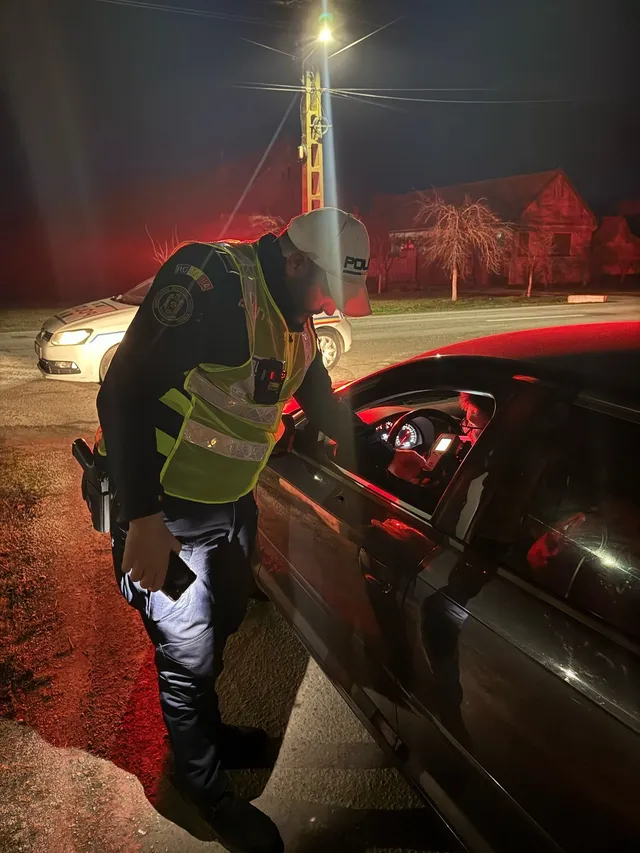Un agent de poliție cu vestă reflectorizantă se apleacă spre fereastra mașinii unui vehicul în timpul nopții.