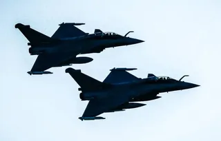Două avioane de luptă siluete zboară în formare pe un cer deschis.