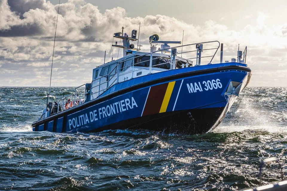 O barcă albastră cu inscripția POLITIA DE FRONTIERA navighează pe un lac sau mare sub un cer înnorat.