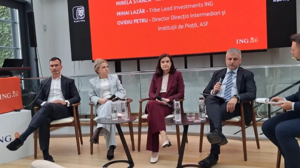 Patru persoane stau așezate pe scaune într-o sală, în fața unui ecran mare cu text pe fundal roșu.